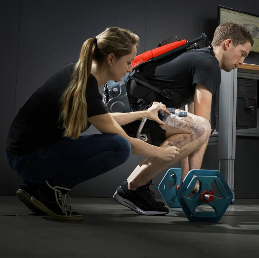 A male subject wearing the German Bionic Apogee Exoskeleton, an advanced exoskeleton suit, is performing a squat while lifting a hexagonal dumbbell. – Now available at MTN Shop EU.
