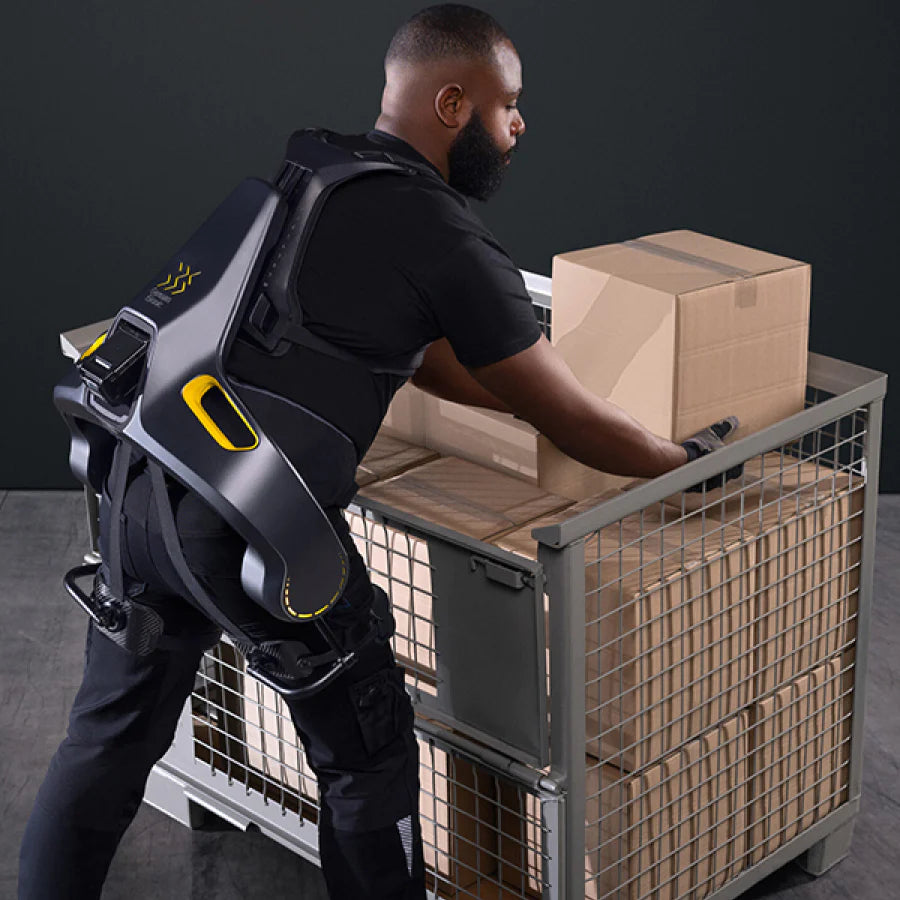 A man wearing the German Bionic Apogee exoskeleton while lifting a cardboard box from a metal cart, highlighting the device’s assistance in reducing strain during repetitive lifting tasks. – Now available at MTN Shop EU.