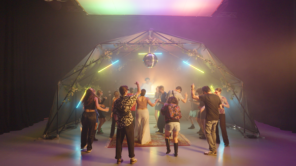 Konligo Fastival event structure with black backdrop and black frame decorated with flowers and neon lights hosting a lively indoor dance party with DJ and disco ball, now available on MTN SHOP US.