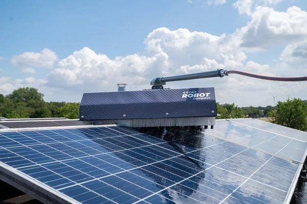 Robot cleaning solar panels on a clear day with blue sky and clouds.