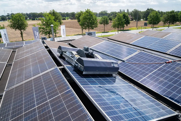 Solar panels on a roof with a tractor in the foreground, surrounded by trees and open fields.