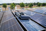 Solar panels on a roof with a tractor in the foreground, surrounded by trees and open fields.
